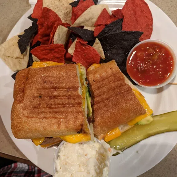 Grilled panini sandwich served with tortilla chips and pickle